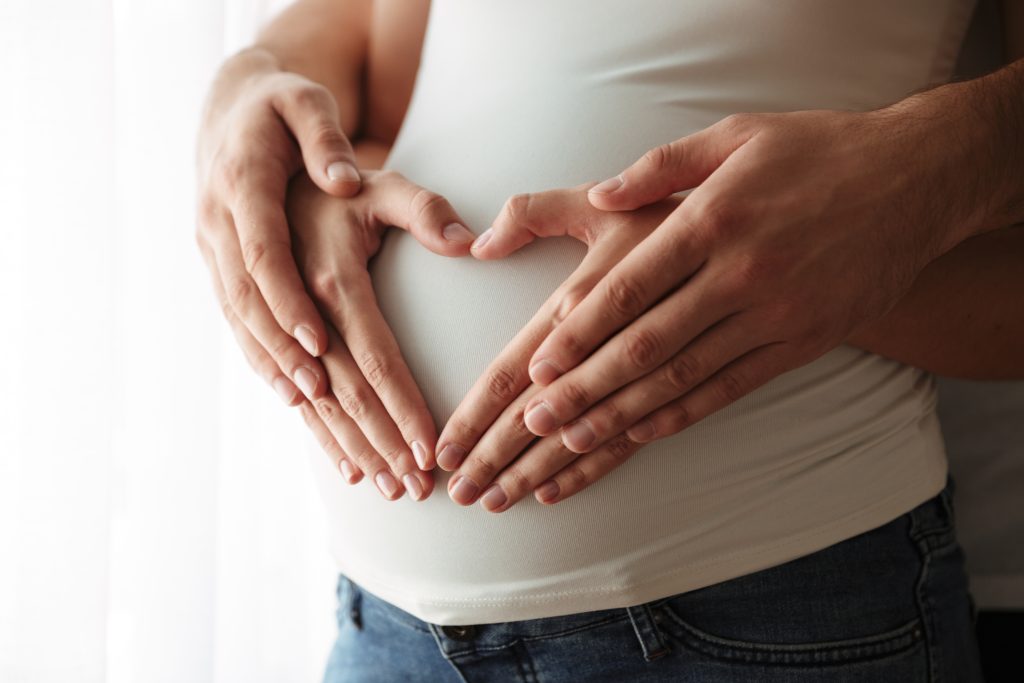 Pareja colocando las manos sobre el vientre simbolizando fertilidad, maternidad y planificación reproductiva
